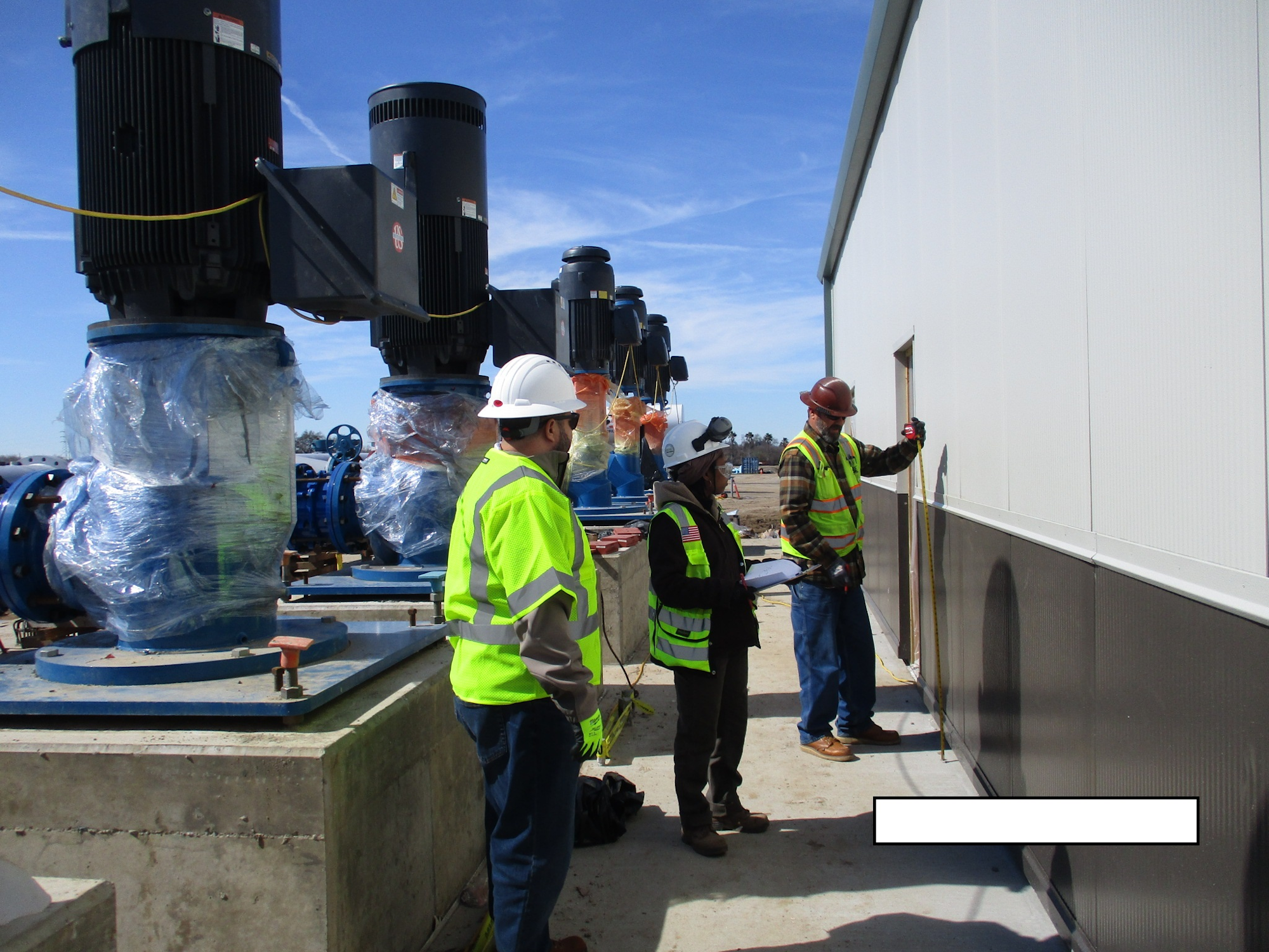 Workers in safety gear inspecting equipment at an industrial site.
