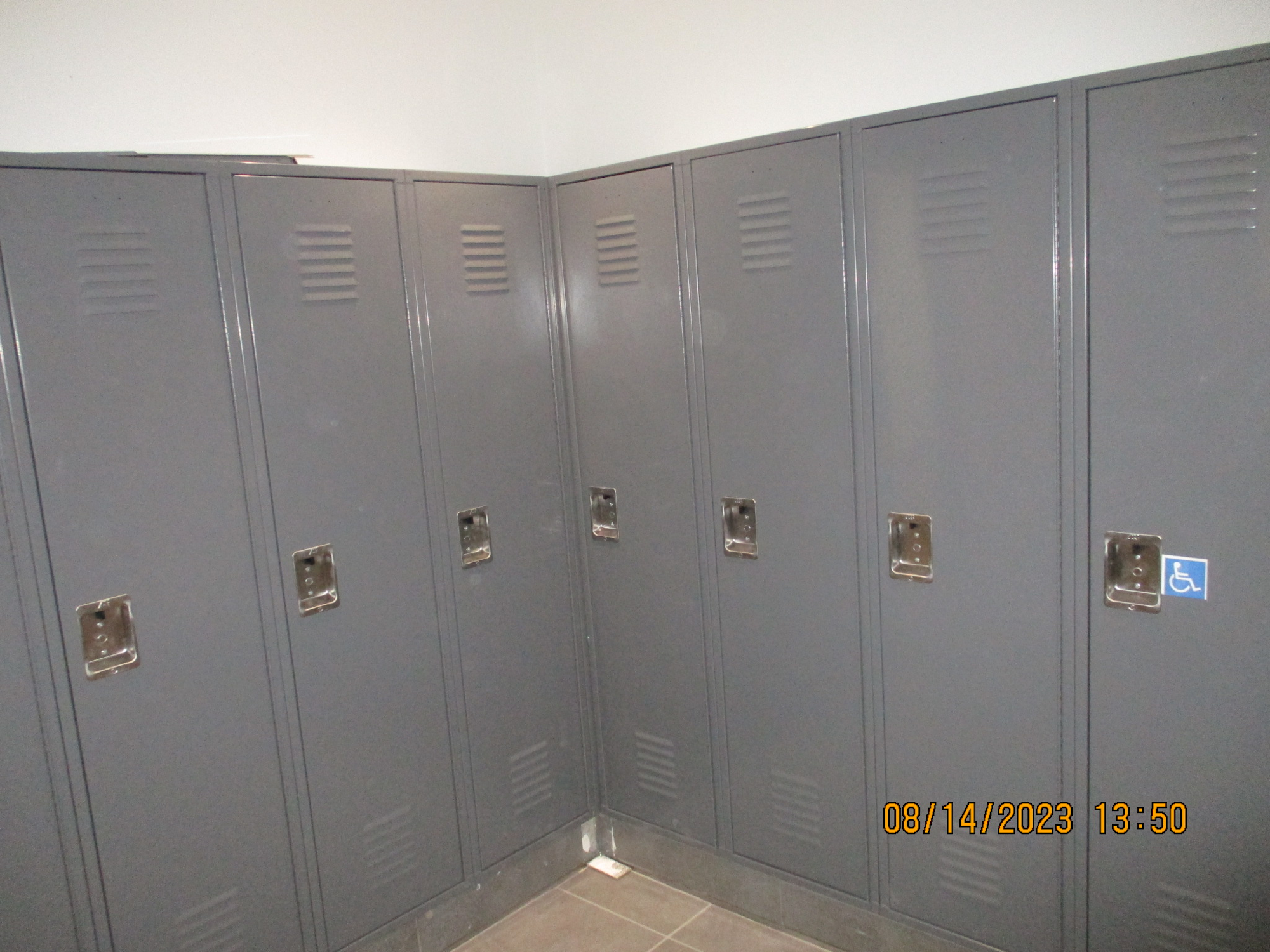 A row of gray lockers with combination locks, one with a handicap sign.