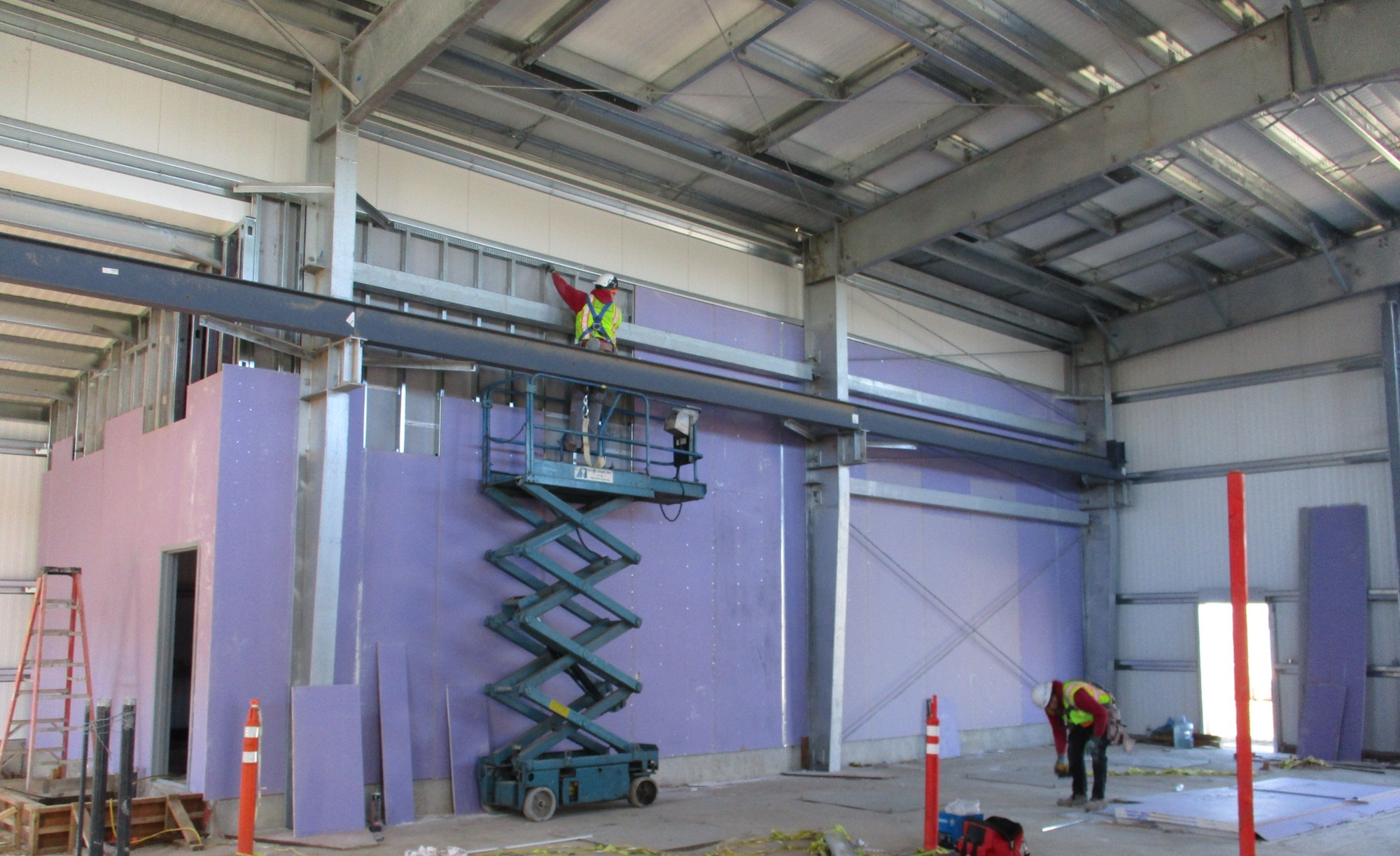 A construction site with workers, scissor lift, insulation panels, and steel structure.