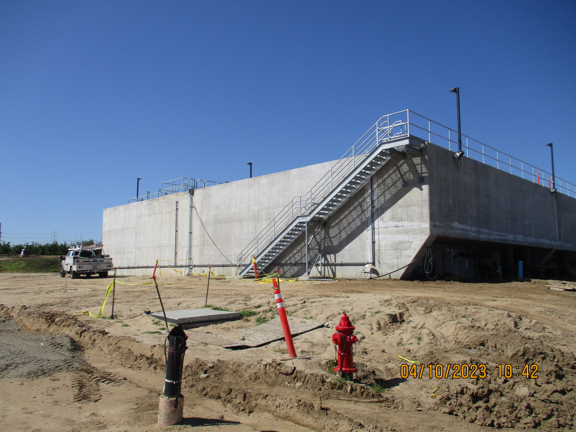 A large concrete structure with stairs, under clear skies at a construction site. A utility truck and a fire hydrant are visible.