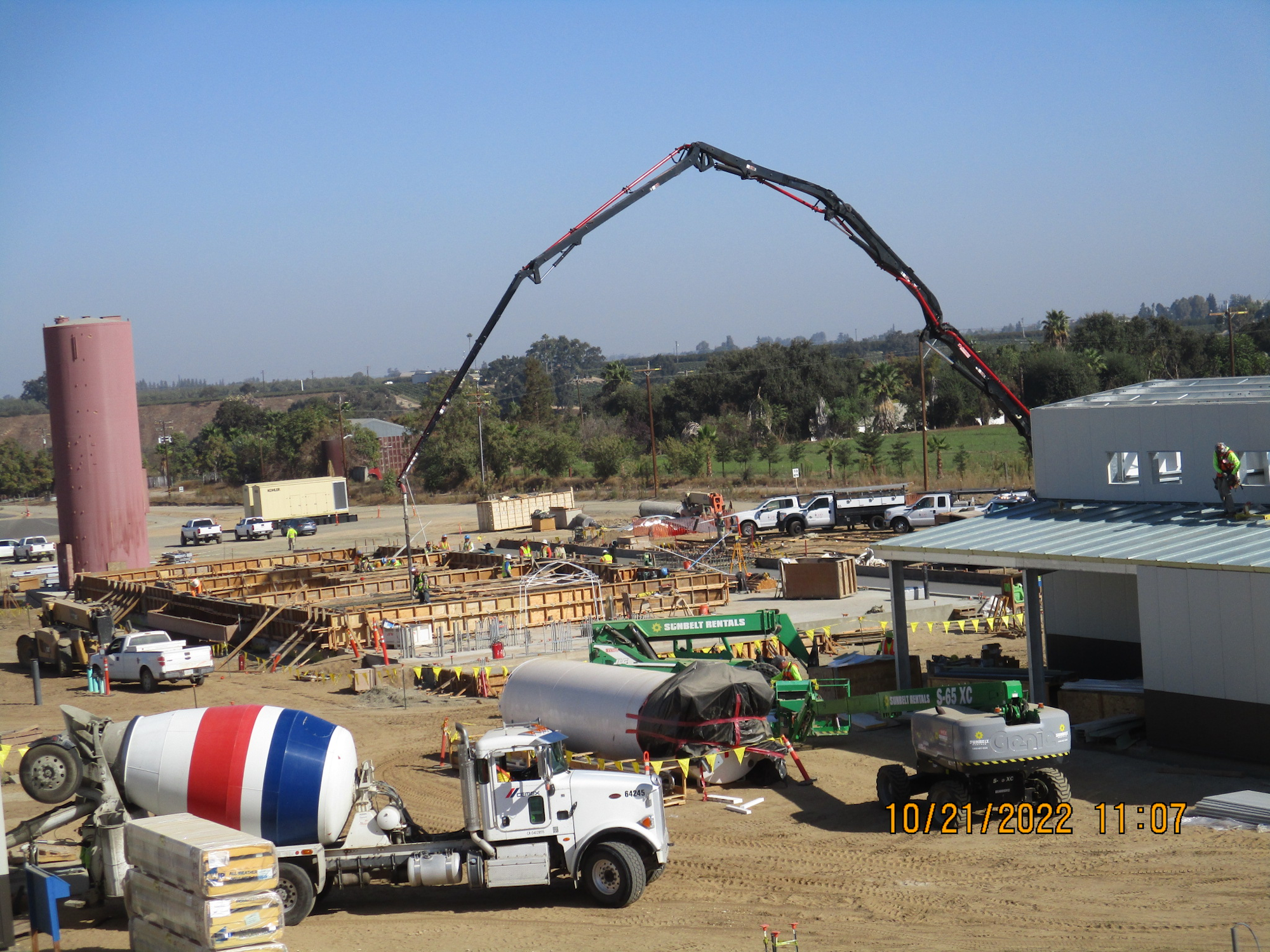 A construction site with a concrete pump truck, workers, and various construction equipment.