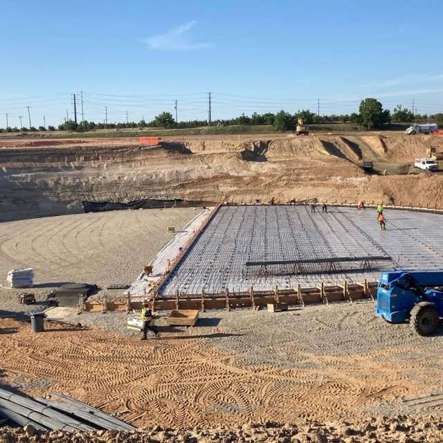 A construction site with workers laying a large reinforced concrete foundation.