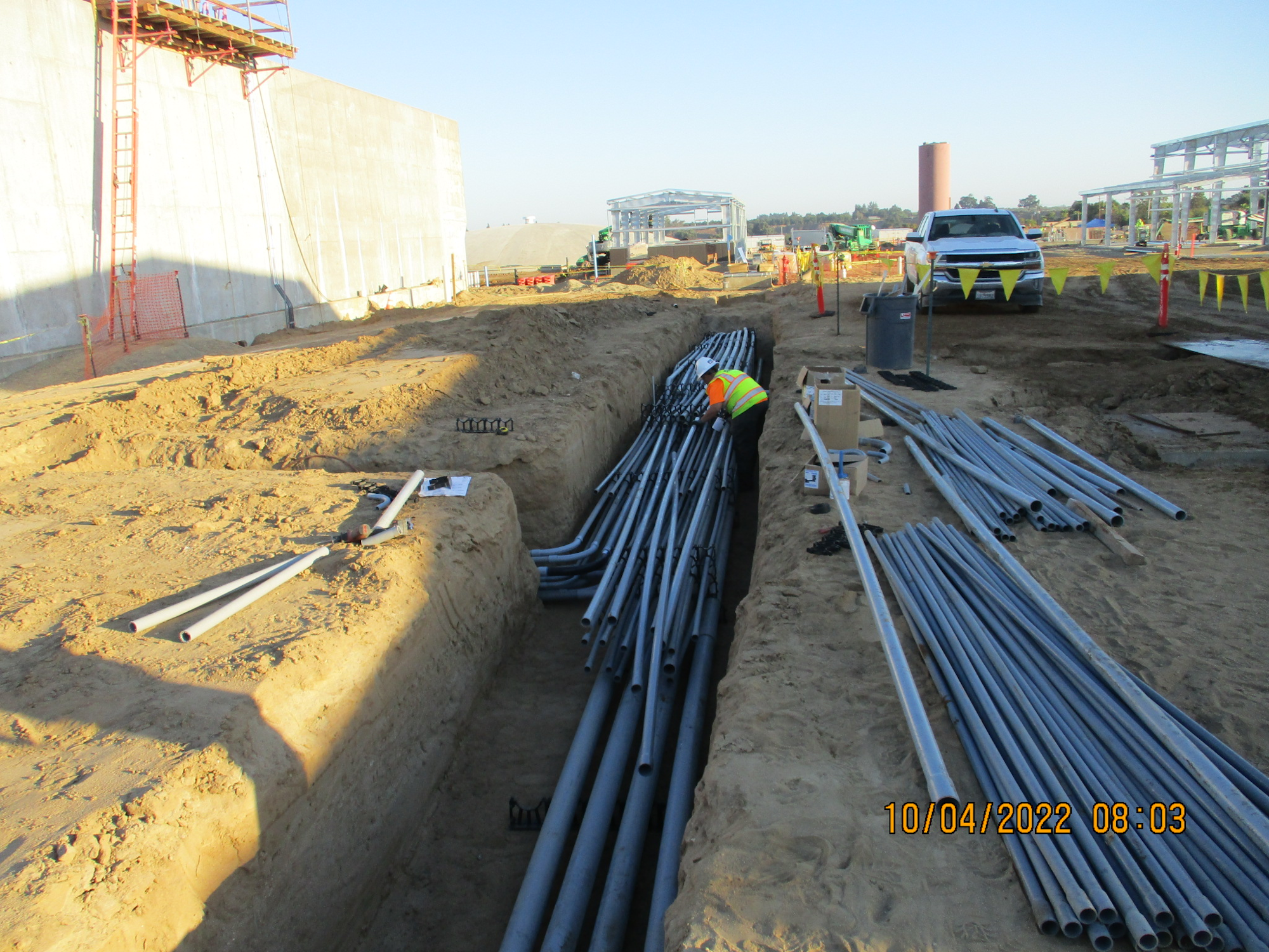 Construction site with trenches, pipes, worker, and a pickup truck.
