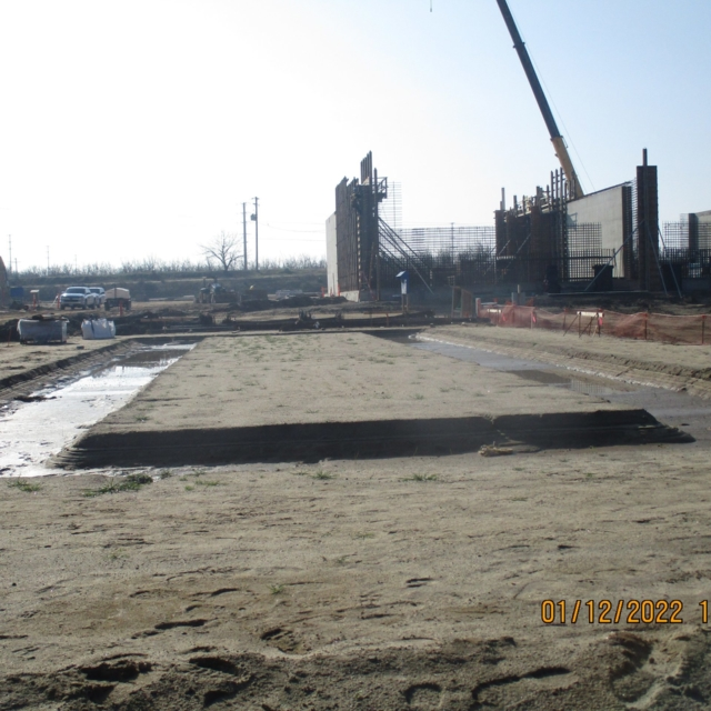 Construction site with foundational work, concrete structures, a crane, and building materials under a clear sky.