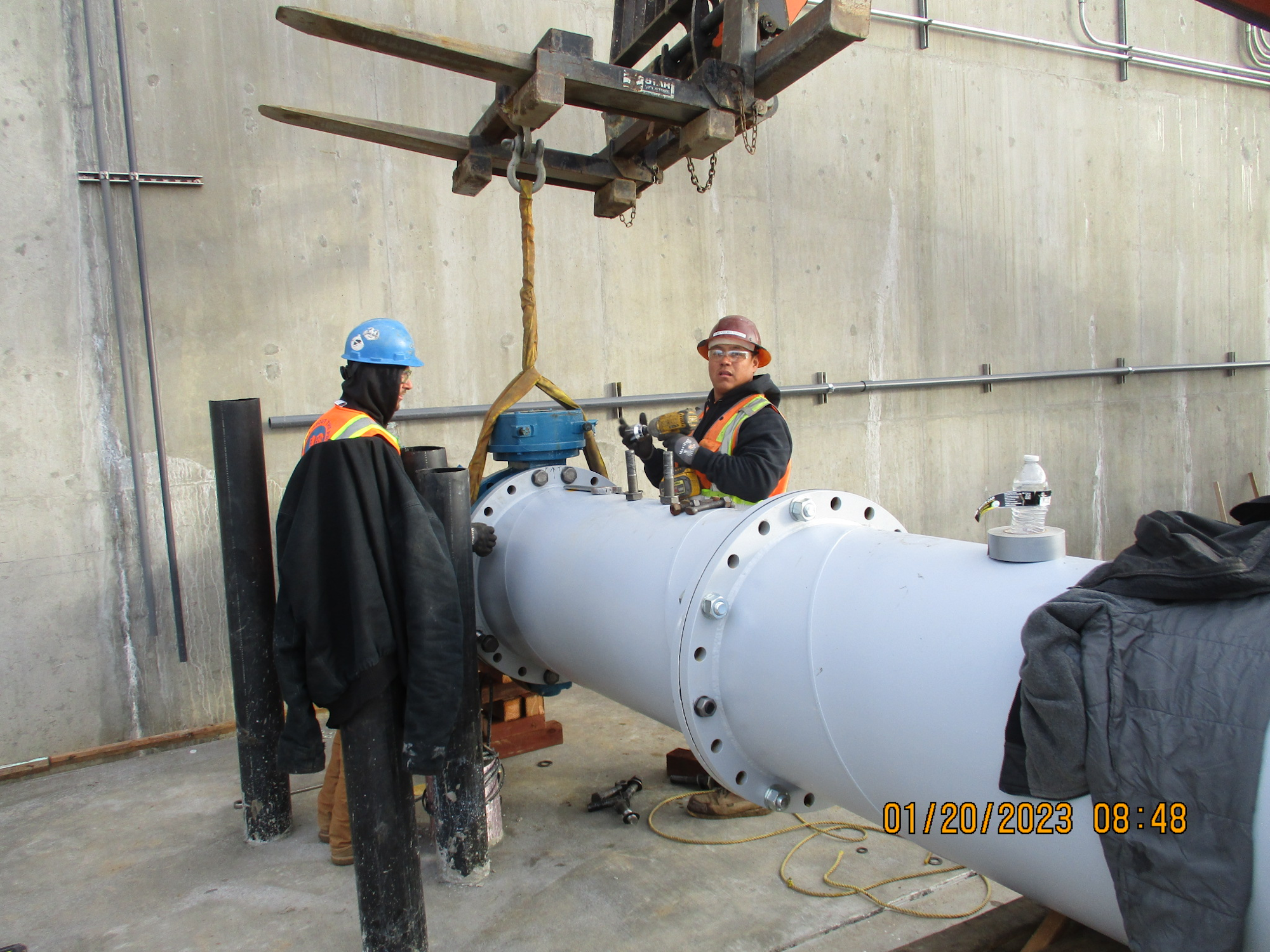 Two workers with hard hats near a large pipe, possibly on a construction site.
