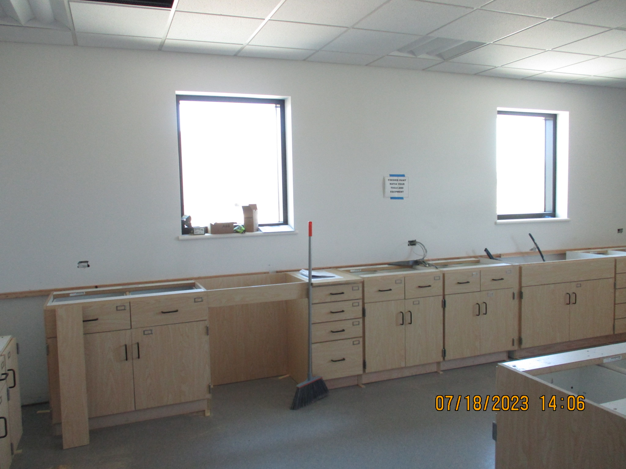 Empty laboratory with wooden cabinets, countertops, broom, and windows.