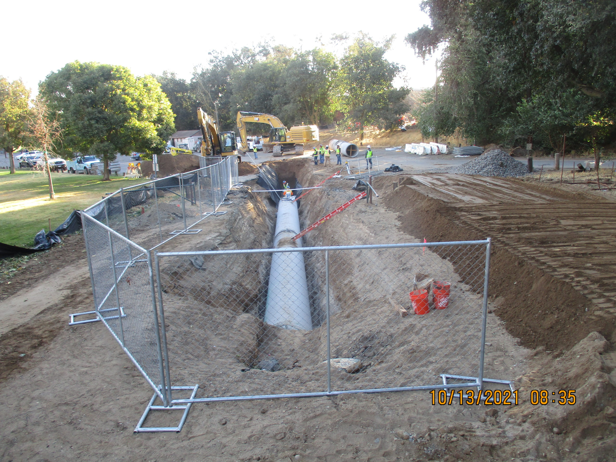 A construction site with an excavated trench, pipes, heavy machinery, and workers.