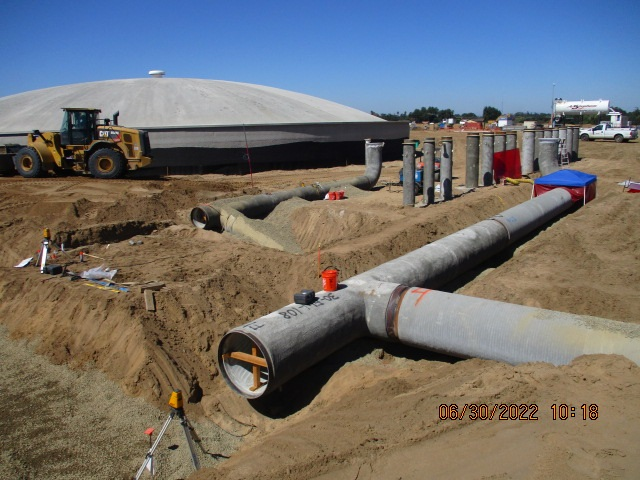 Construction site with large pipes and a dome structure in the background.