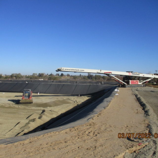 Construction site with machinery, conveyor belt, and barrier liner installation.