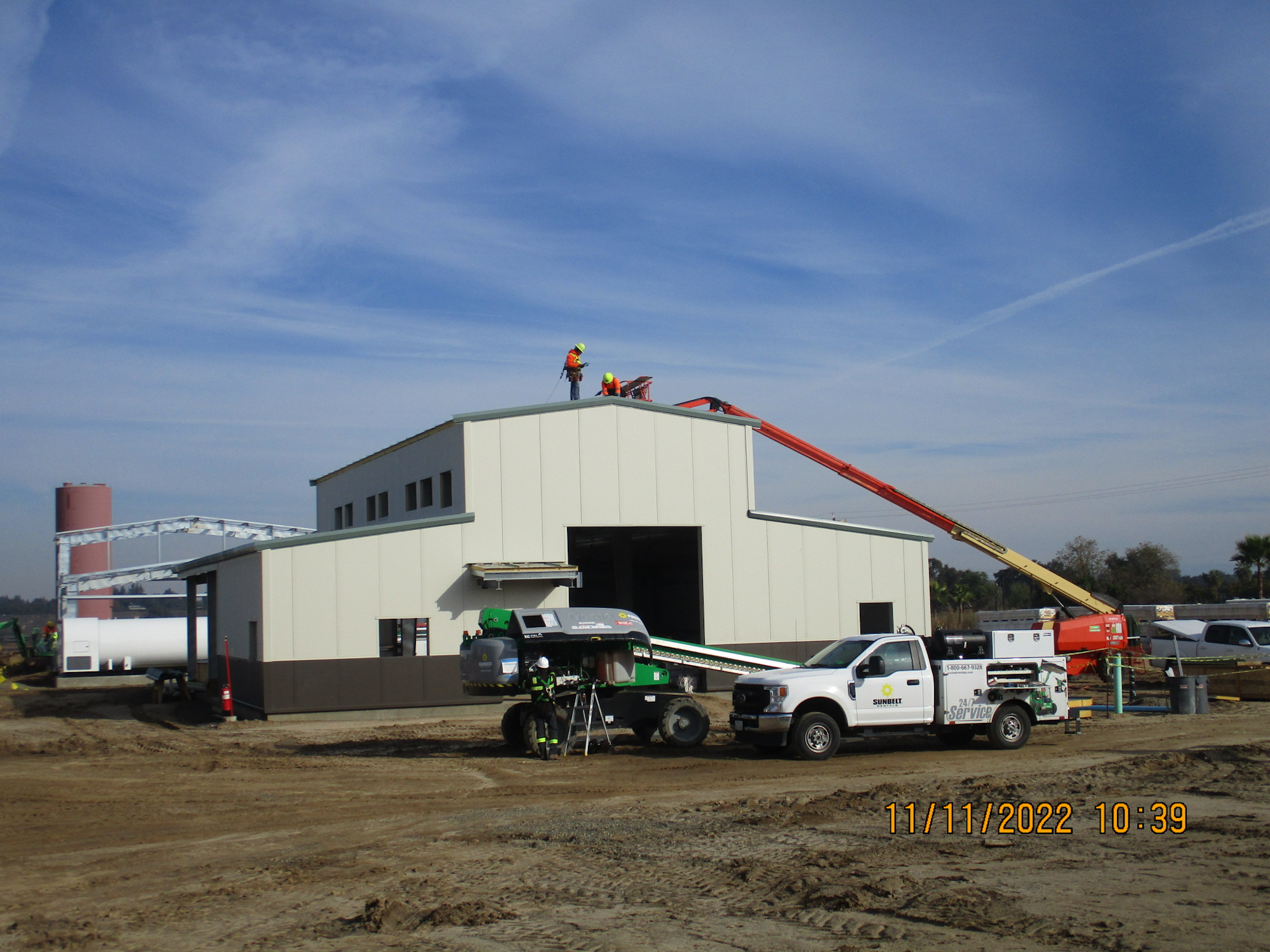 Construction site with workers on rooftop, vehicles below, and a clear blue sky.