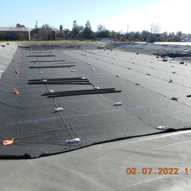 Large area covered with geotextile fabric, pipes and sandbags for construction or environmental protection.