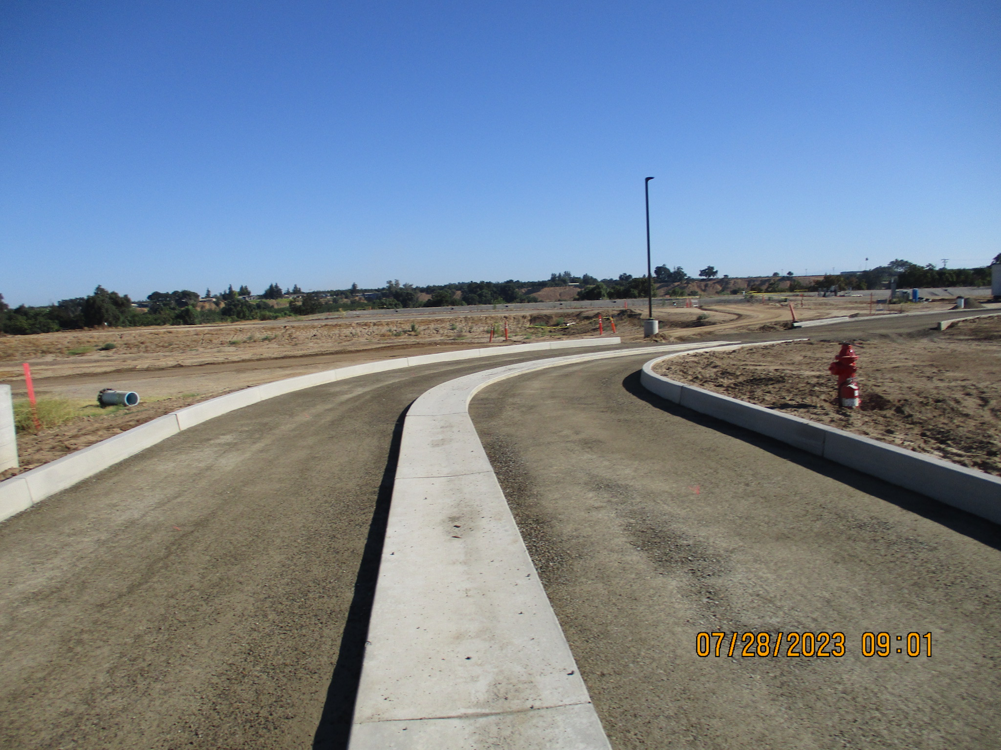 Curved road under construction, clear blue sky, no people, timestamped 07/28/2023.