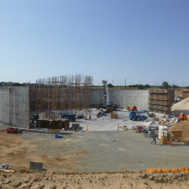 Construction site with concrete structures, scaffolding, and equipment under a clear sky.