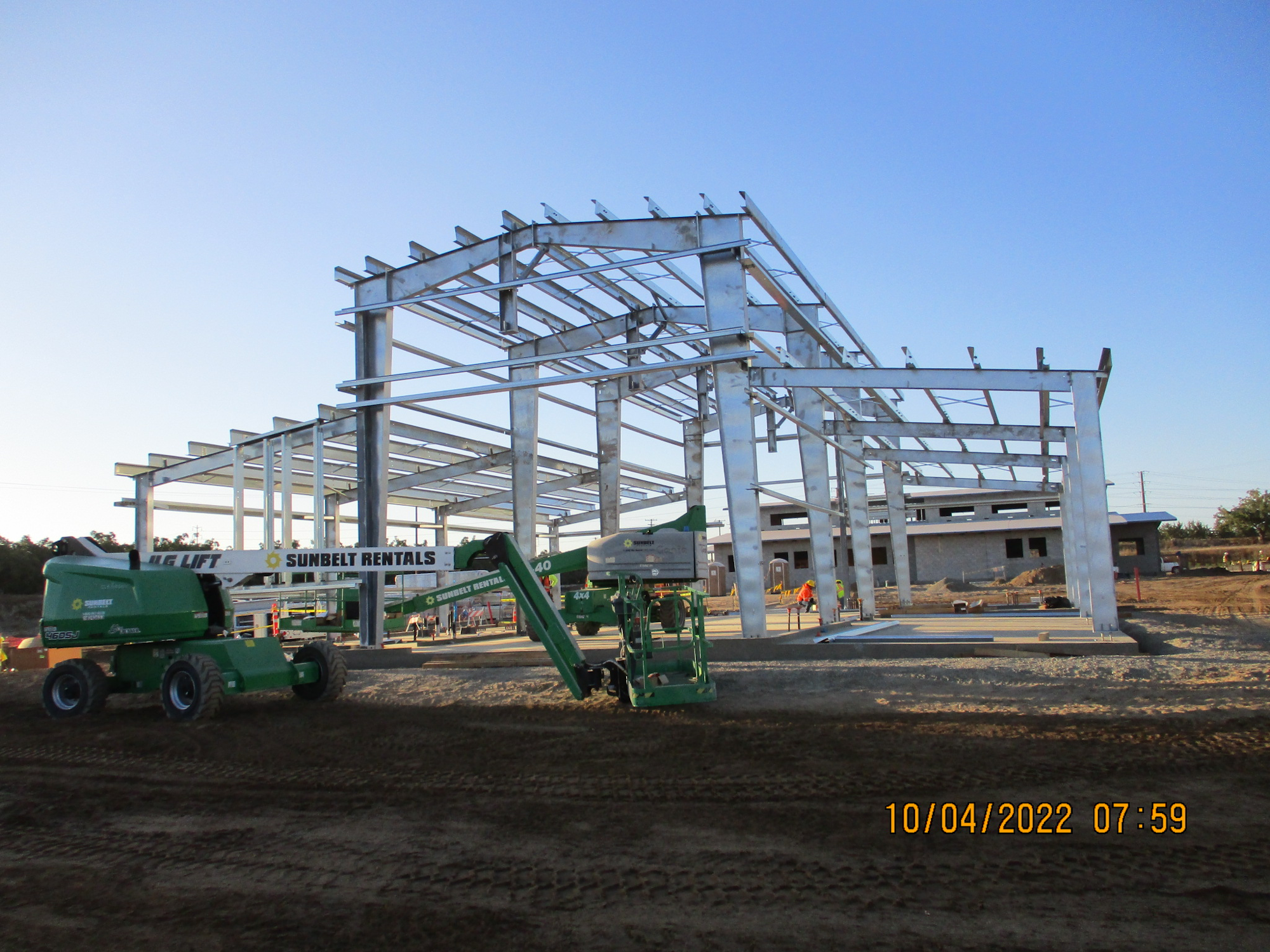 Steel structure under construction with lifting equipment on site.