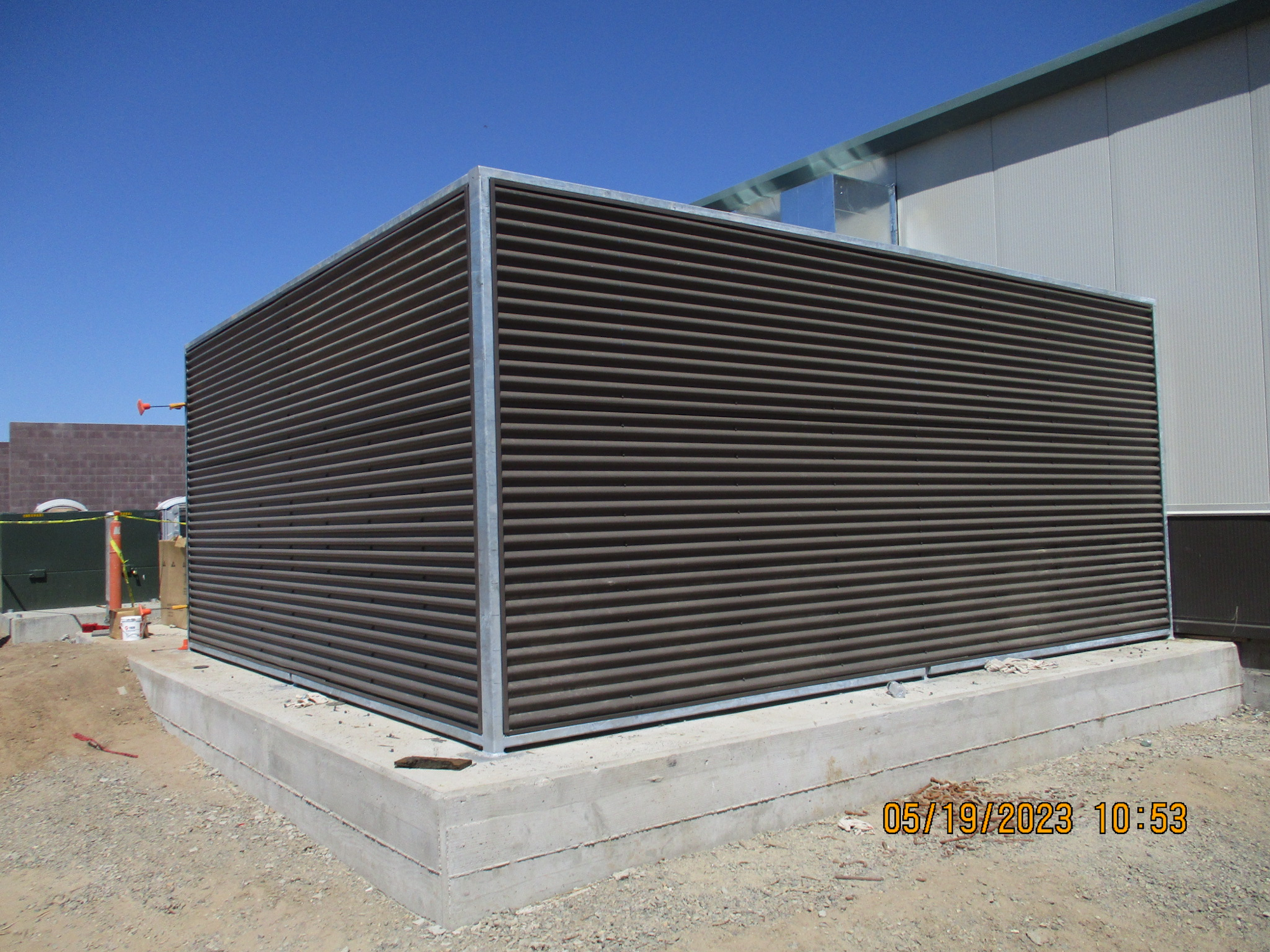 A large industrial louvred ventilation structure on a concrete base, under a clear sky.