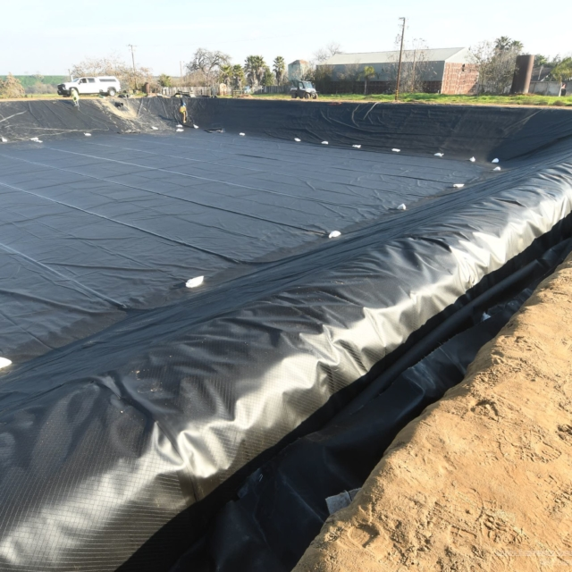 A large containment area lined with black geotextile fabric, possibly for environmental protection or construction.