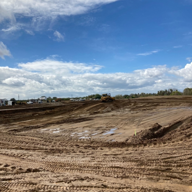 Construction site with earthmover, tire tracks on soil, and cloudy sky.