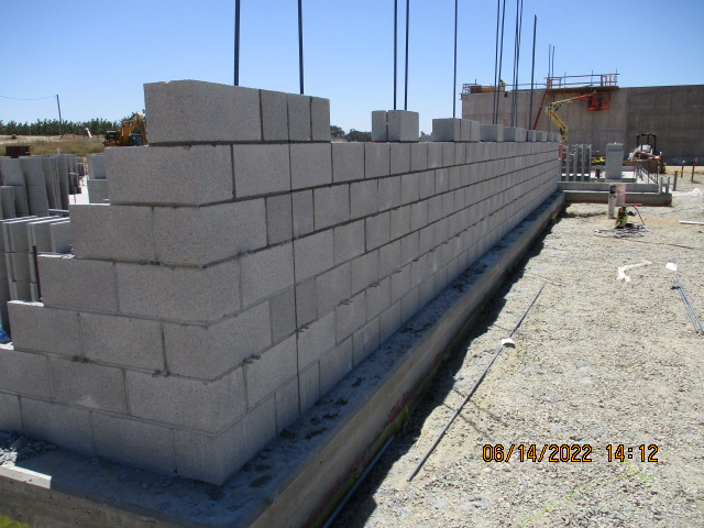 Cinder block wall construction site, with steel rods and construction equipment in the background.