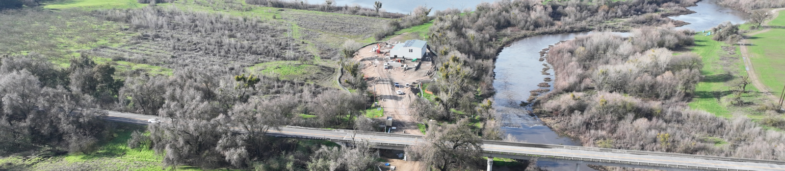Aerial view of a bridge over a river, adjacent buildings, roads, and greenery.