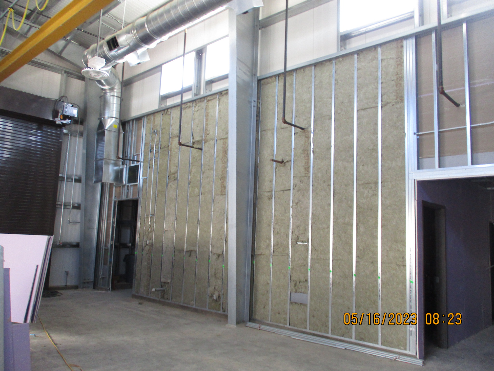 Exposed insulation between metal studs at a construction site, with ductwork overhead.