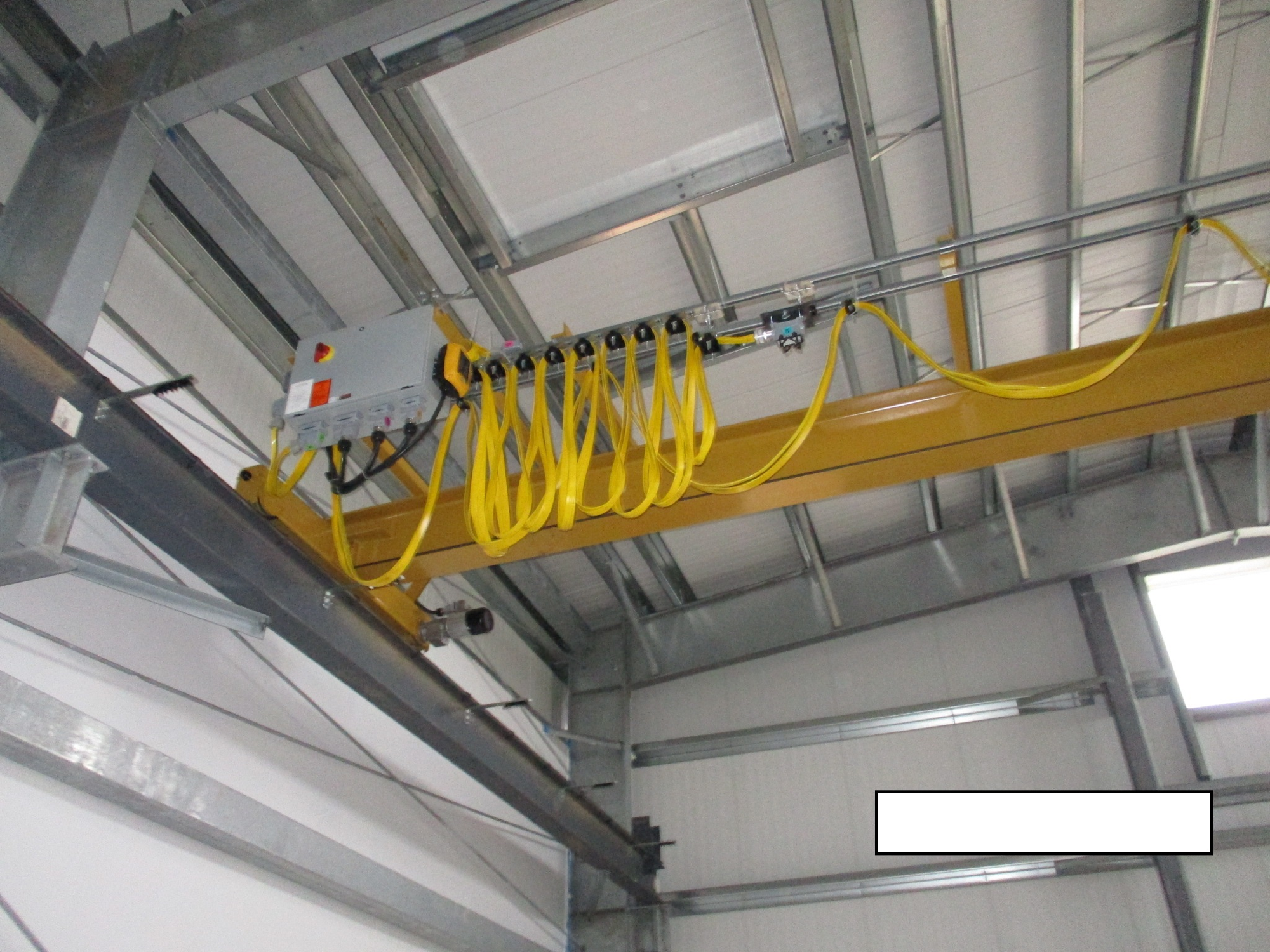 Overhead crane with electrical panel and festoon cable system in an industrial setting.