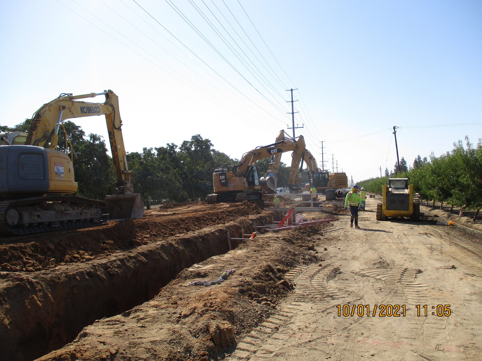 Construction site with excavators, a trench, a roller, and a worker wearing high visibility clothing.