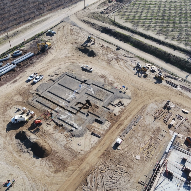 Aerial view of a construction site with foundation work underway, vehicles, and equipment scattered around.