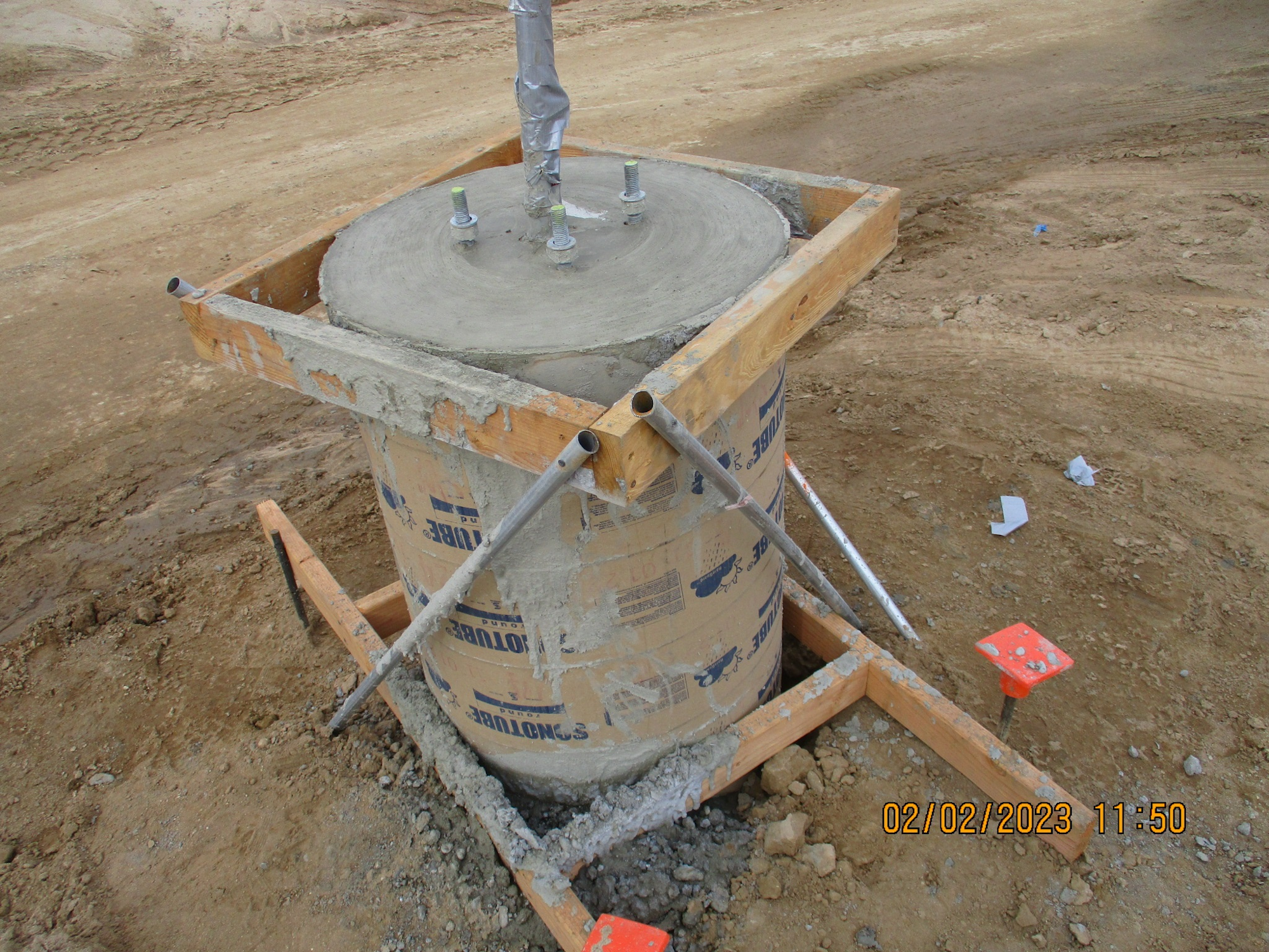 Concrete footing construction with formwork, anchor bolts, and horizontal rebar on a dirt site.