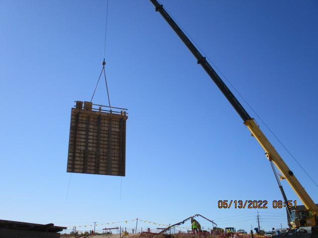 A crane lifting a large object at a construction site under a clear blue sky.