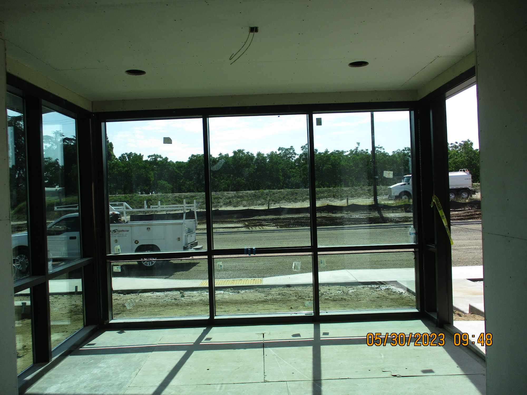 Interior view through large windows at a construction site with vehicles outside.