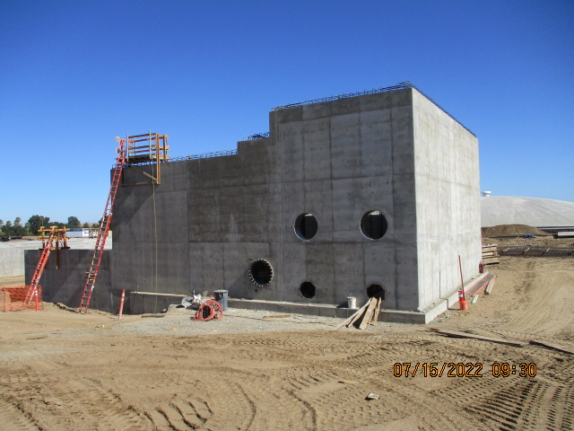 Concrete structure at a construction site with openings, ladders, and construction material under a clear sky.