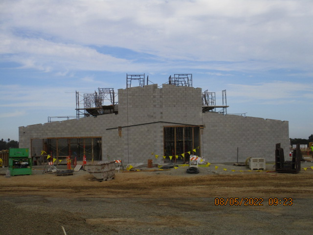 A construction site with a partially built cinder block building and scaffolding under a cloudy sky.