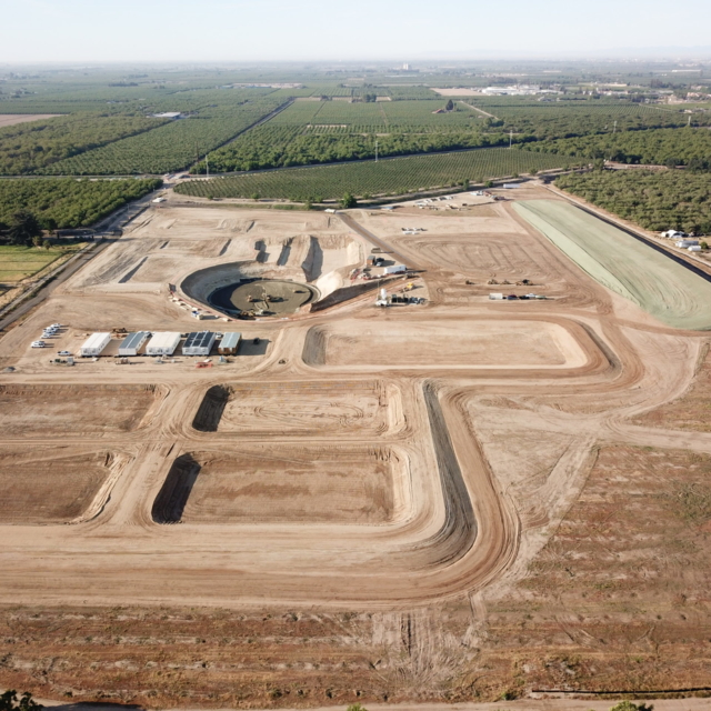 Aerial view of a construction site with dirt tracks and a round structure, surrounded by vegetation.
