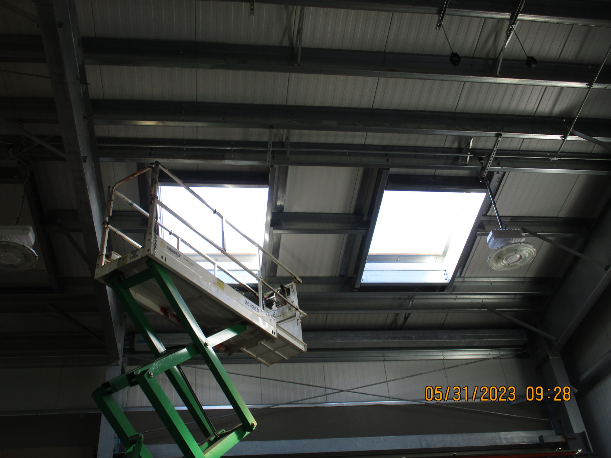 An elevated platform lift inside an industrial building with skylights and exposed ceiling structures.