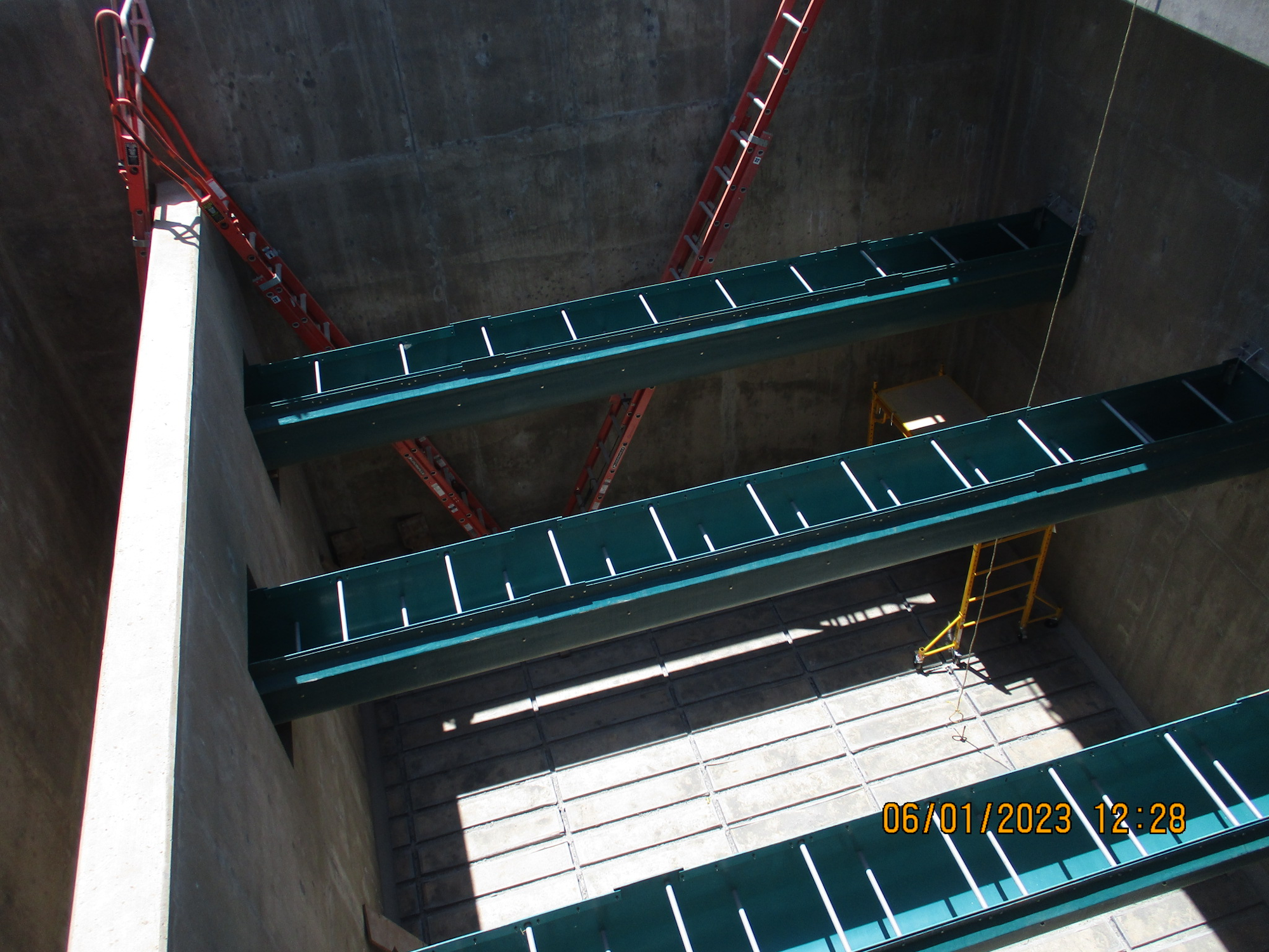 Steel beams inside a concrete structure under construction with ladders for access.