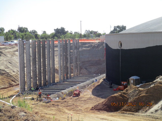 Construction site with workers, large retaining walls, and excavation.