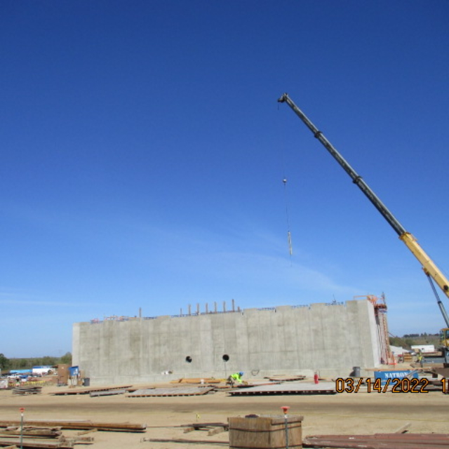 A construction site with a crane, concrete walls, and clear blue sky.