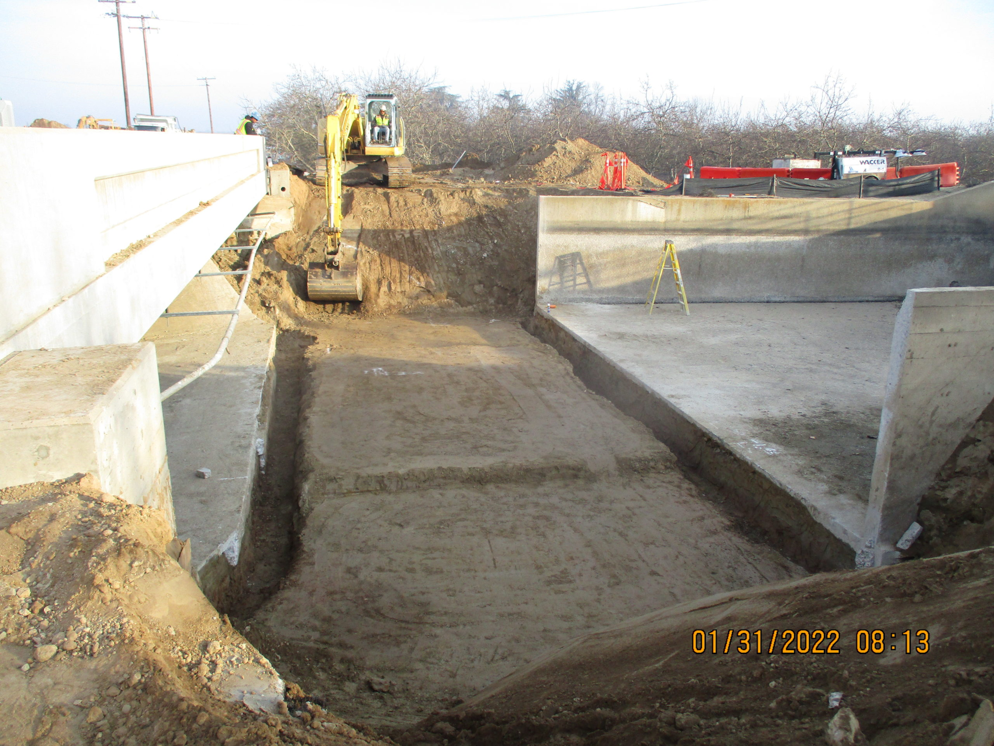 Construction site with an excavator, concrete walls, and a dug trench.