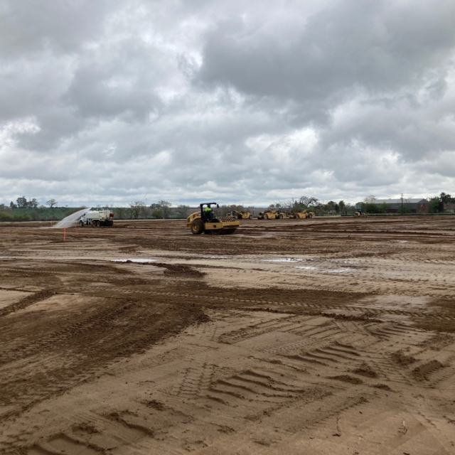 Construction site with heavy machinery and muddy ground under cloudy skies.