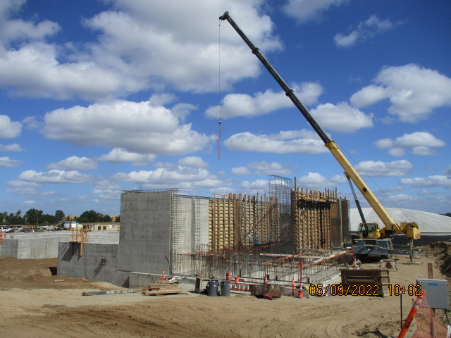 A construction site with a crane, concrete walls, and wooden formwork under a blue sky with clouds.