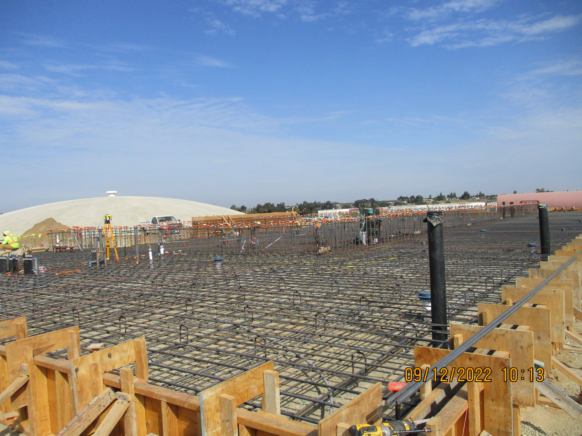 Construction site with rebar grid for concrete, dome structure in the background, clear sky, timestamped 09/12/2022 10:13.