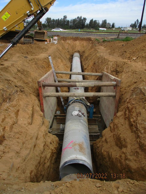 Large pipe in a trench, supported by trench shields, construction site.