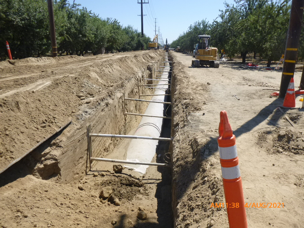 A trench with concrete foundations and construction safety cones, with machinery in the background.