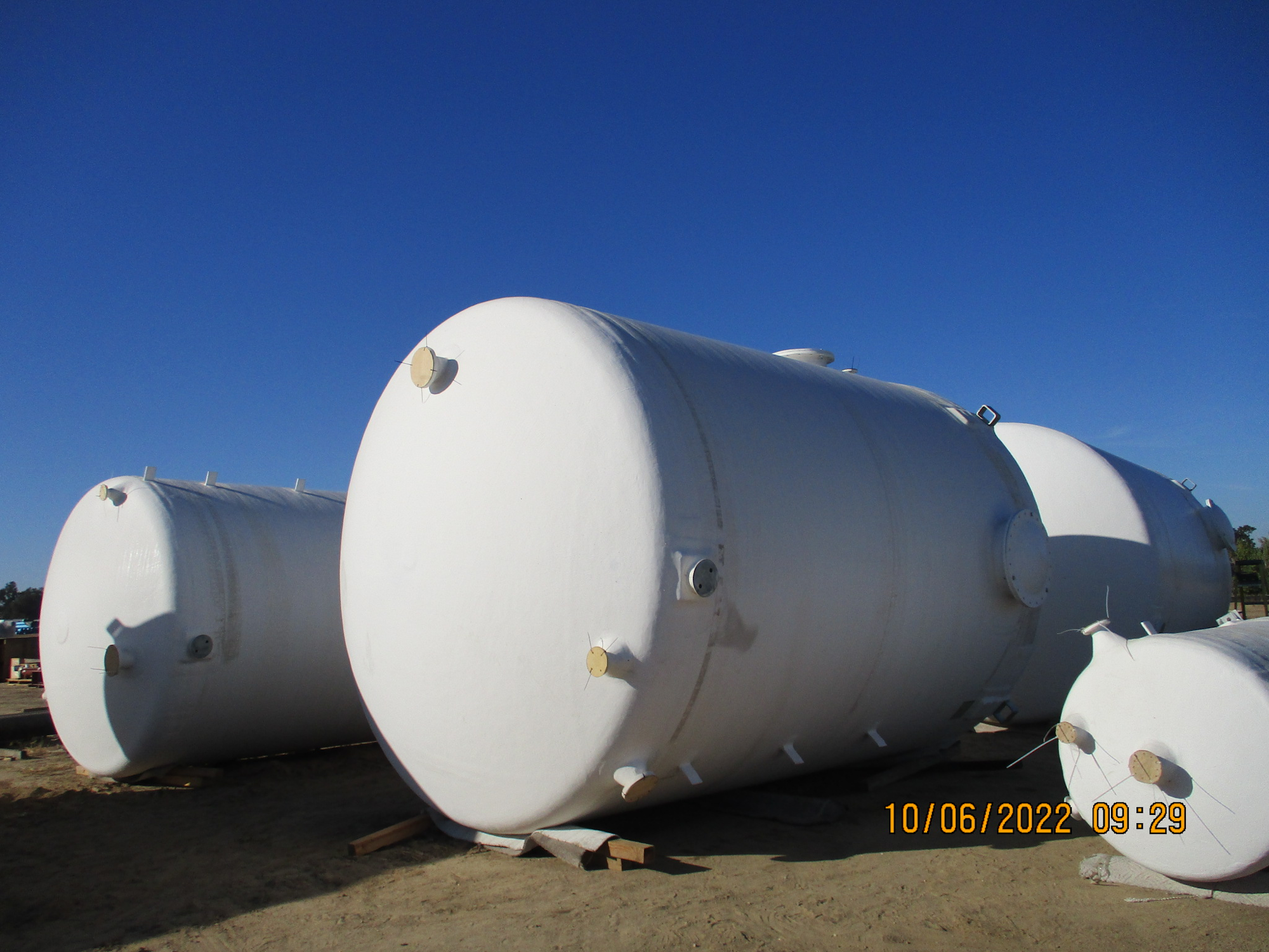Large white storage tanks on wooden supports against a blue sky.