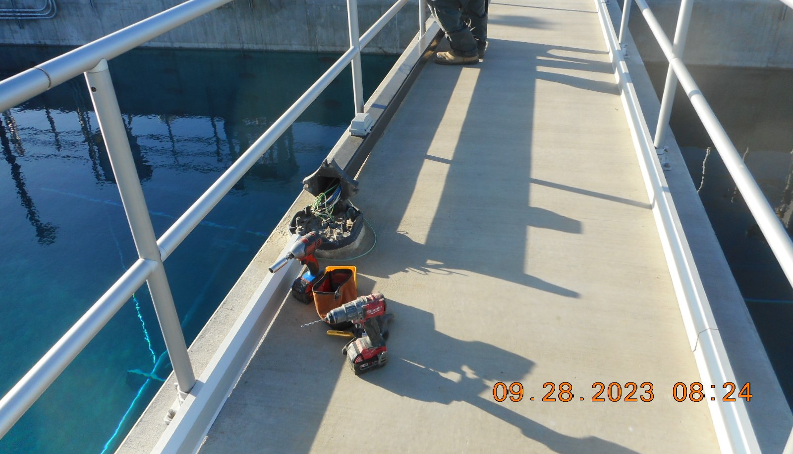 A walkway with railings, electrical wiring, tools, and a person's legs.