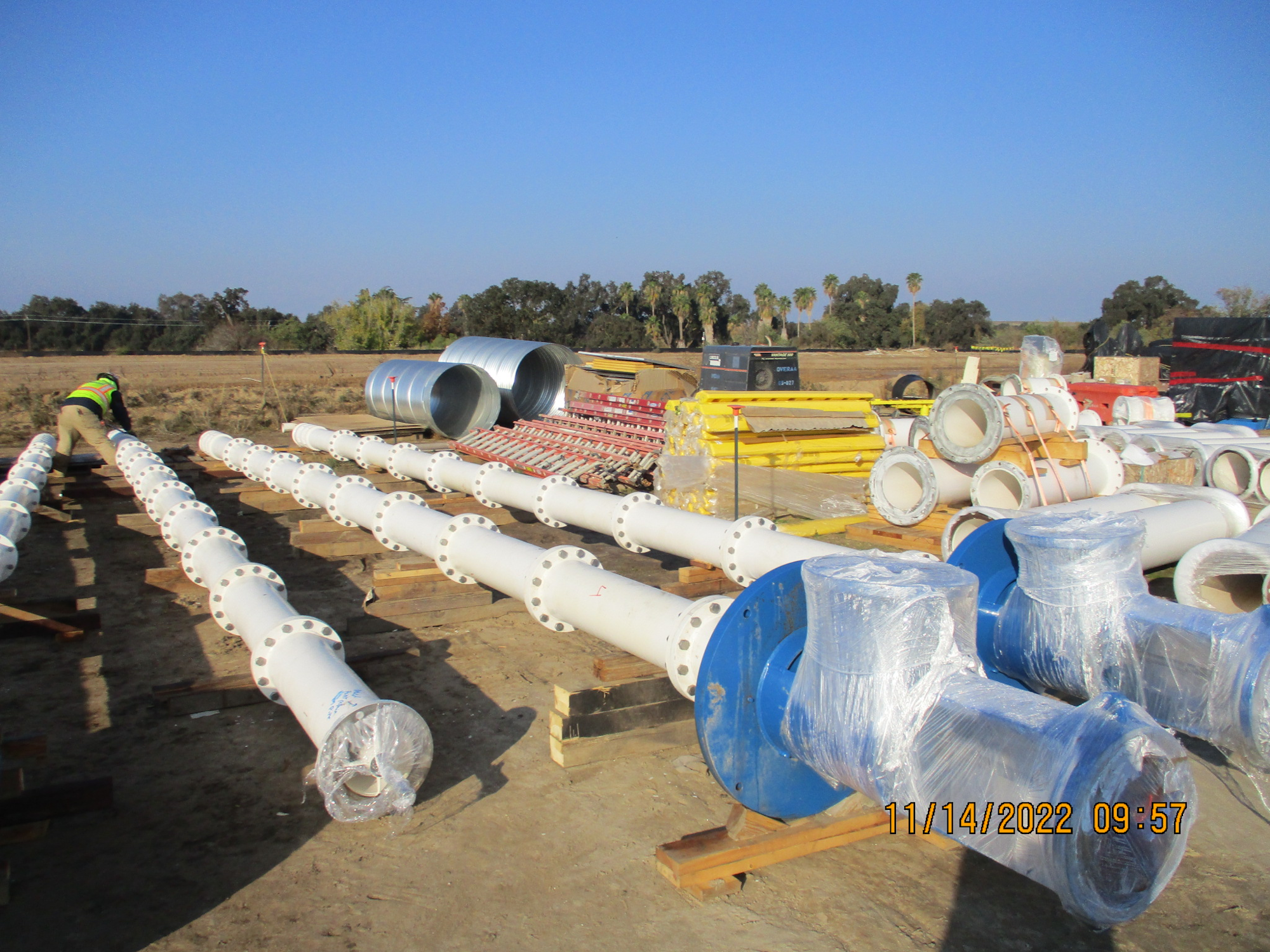 Industrial site storing large pipes and construction materials, with one person visible in hi-vis clothing.