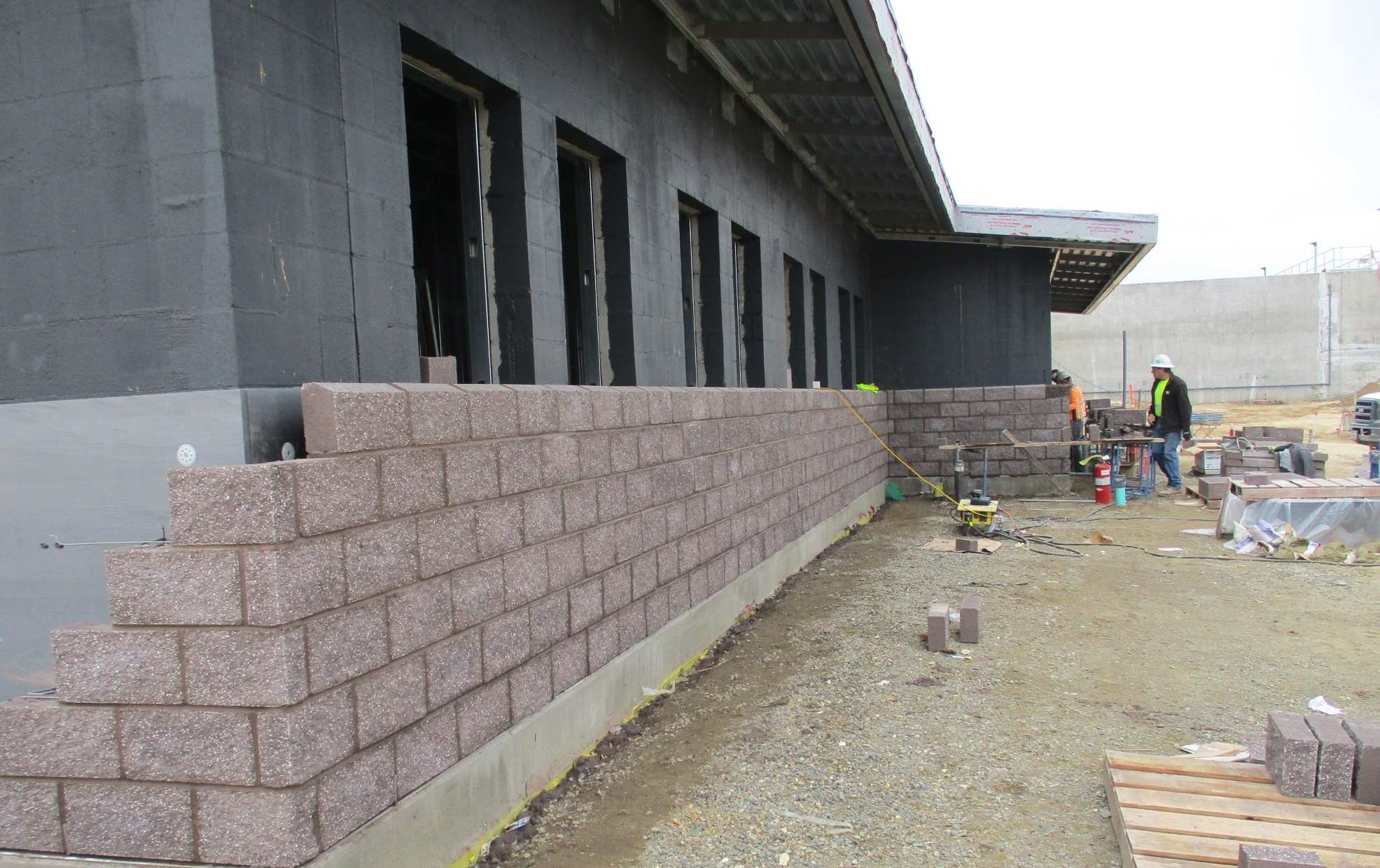 Construction site with workers, cinder block wall in progress, and building materials.