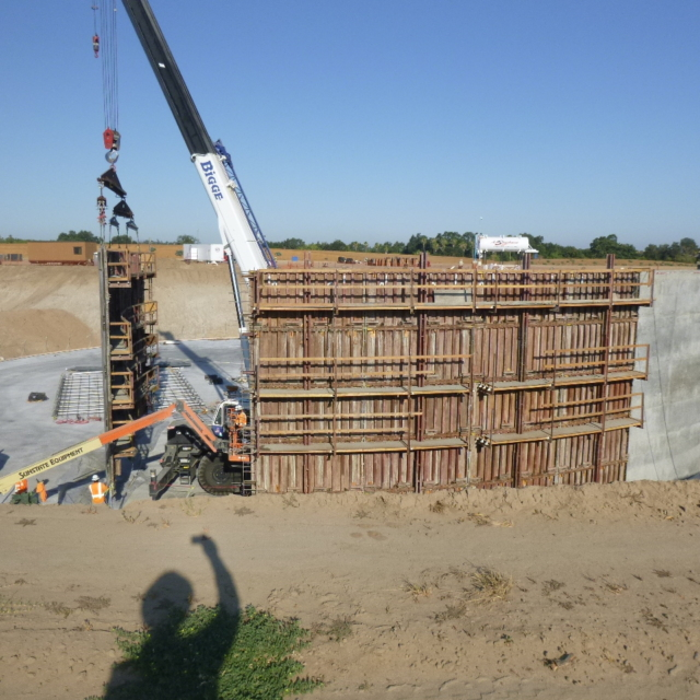 Construction site with a crane, concrete forms, and a person's shadow in the foreground.