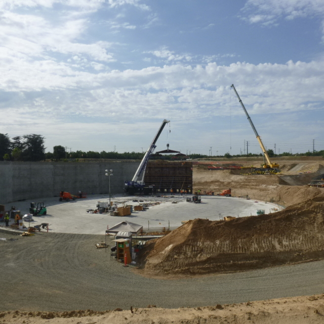 Construction site with cranes, workers, concrete walls, and excavation.
