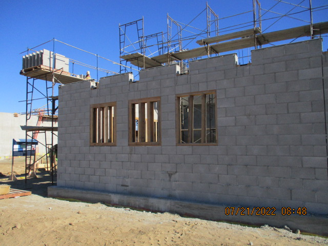 A construction site with a cinder block building, scaffolding, and clear blue sky.